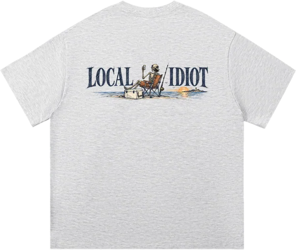 Back: LOCAL IDIOT in navy, a skeleton in a beach chair between the words, beer up, feet on a cooler, sun going down