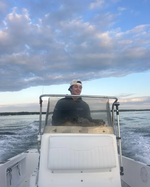 Brandon Bistrian smiling at the wheel of a center-console boat, running across the bay at dusk